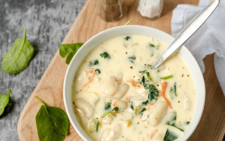 Overhead image of a bowl of chicken gnocchi soup on a wooden cutting board