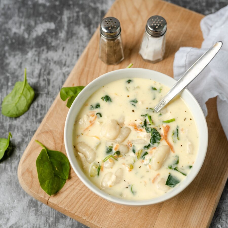 Overhead image of a bowl of chicken gnocchi soup on a wooden cutting board