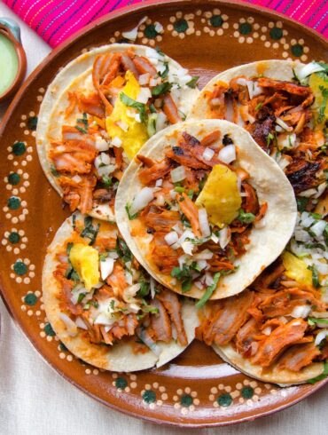 Overhead image of five Pork Al Pastor tacos on a decorative plate