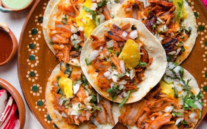 Overhead image of five Pork Al Pastor tacos on a decorative plate