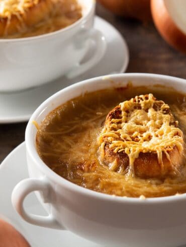 Two white bowls with handles full of Slow Cooker French Onion Soup