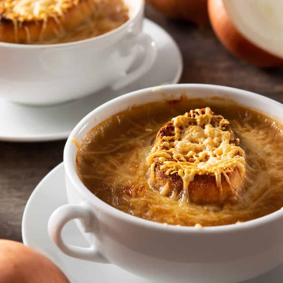 Two white bowls with handles full of Slow Cooker French Onion Soup