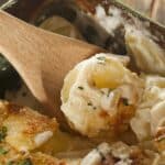 A wooden spoon serving a portion of slow cooker scalloped potatoes