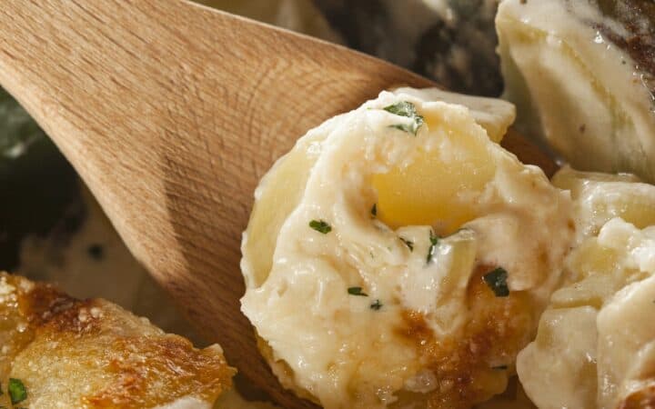 A wooden spoon serving a portion of slow cooker scalloped potatoes