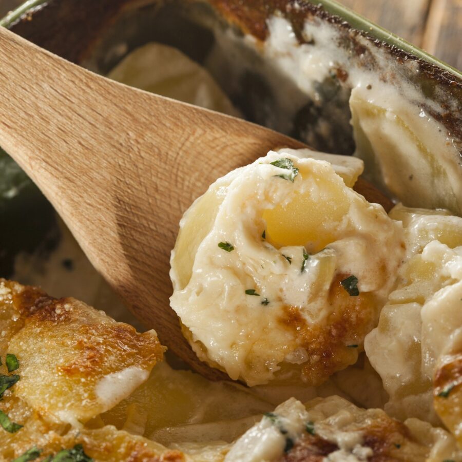 A wooden spoon serving a portion of slow cooker scalloped potatoes