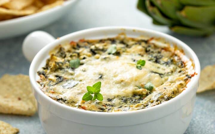 Close up image of crockpot spinach artichoke dip in a white crock