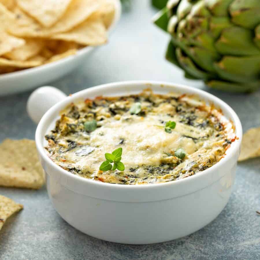 Close up image of crockpot spinach artichoke dip in a white crock