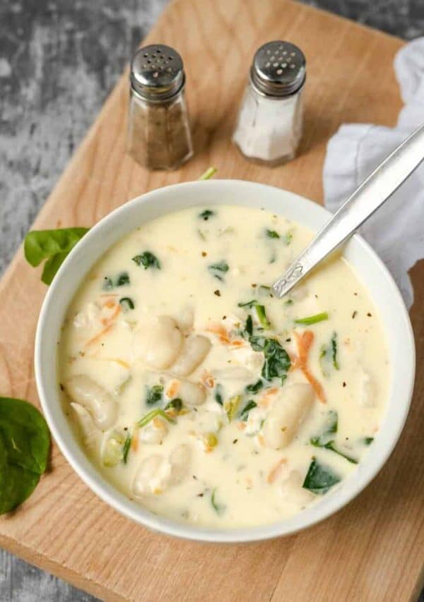 Overhead image of a bowl of chicken gnocchi soup on a wooden cutting board