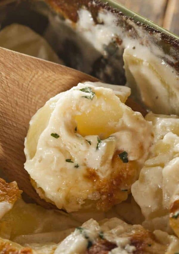 A wooden spoon serving a portion of slow cooker scalloped potatoes