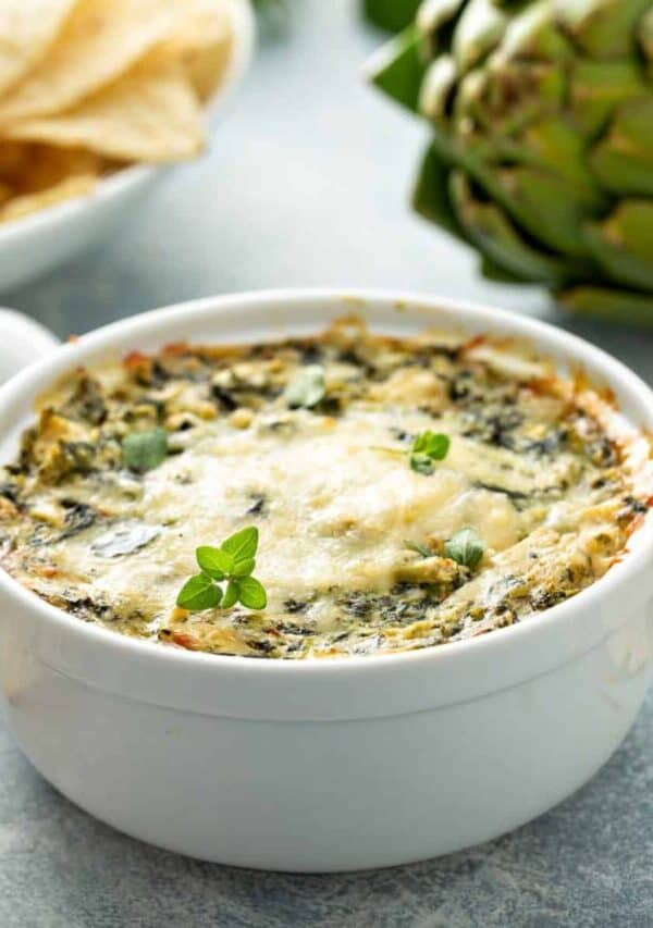 Close up image of crockpot spinach artichoke dip in a white crock