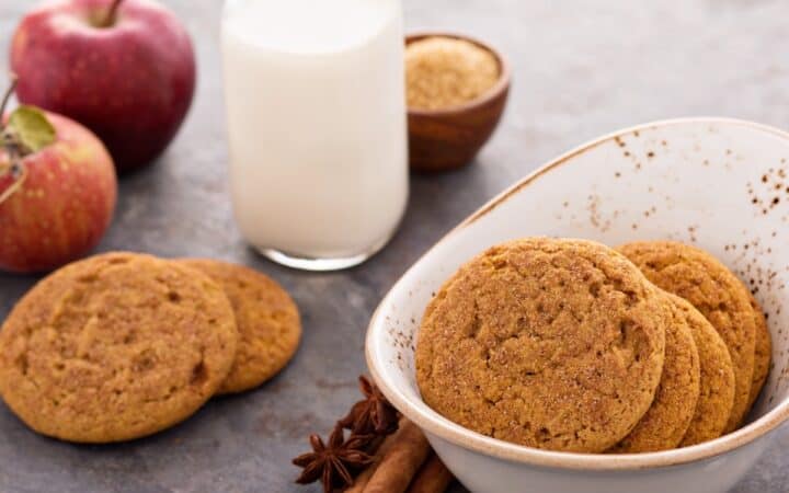 Applesauce Cookies in a white bowl with a glass of milk and more cookies beside it