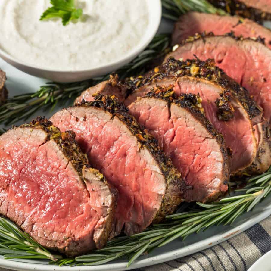 Overhead image of Beef Tenderloin Roast sliced on a bed of herbs