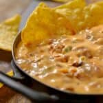 Close up image of chili cheese dip in a skillet with chips dunked in it