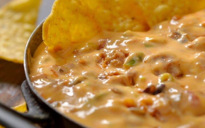 Close up image of chili cheese dip in a skillet with chips dunked in it