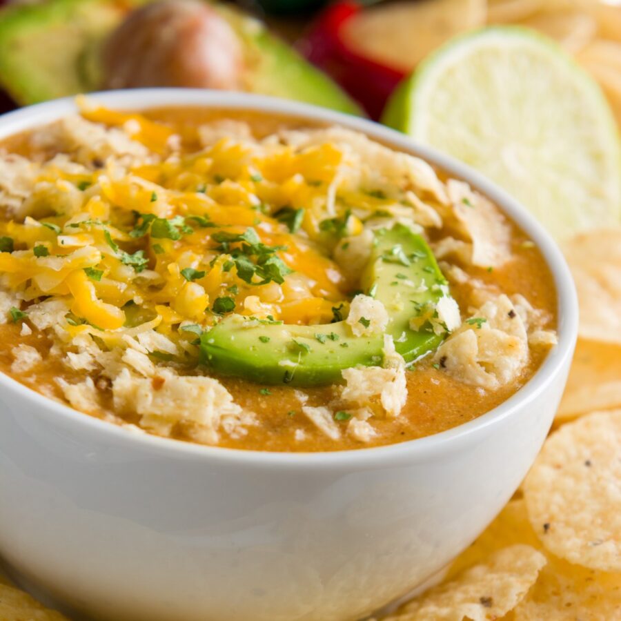 Close up image of Green Chicken Enchilada Soup in a white bowl with chips surrounding it