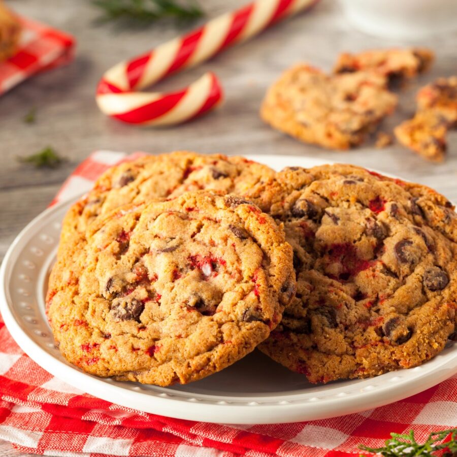 A stack of Peppermint Chocolate Chip Cookies on a white plate with candy canes in the background