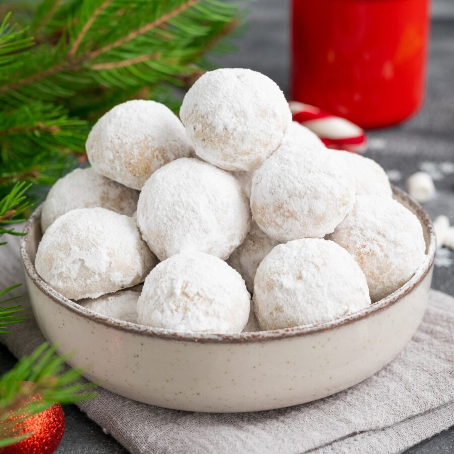 Close up image of Snowball Cookies in a bowl with Christmas decor surrounding it