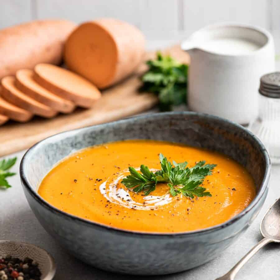 Close up image of sweet potato soup in a bowl with sliced sweet potatoes behind it