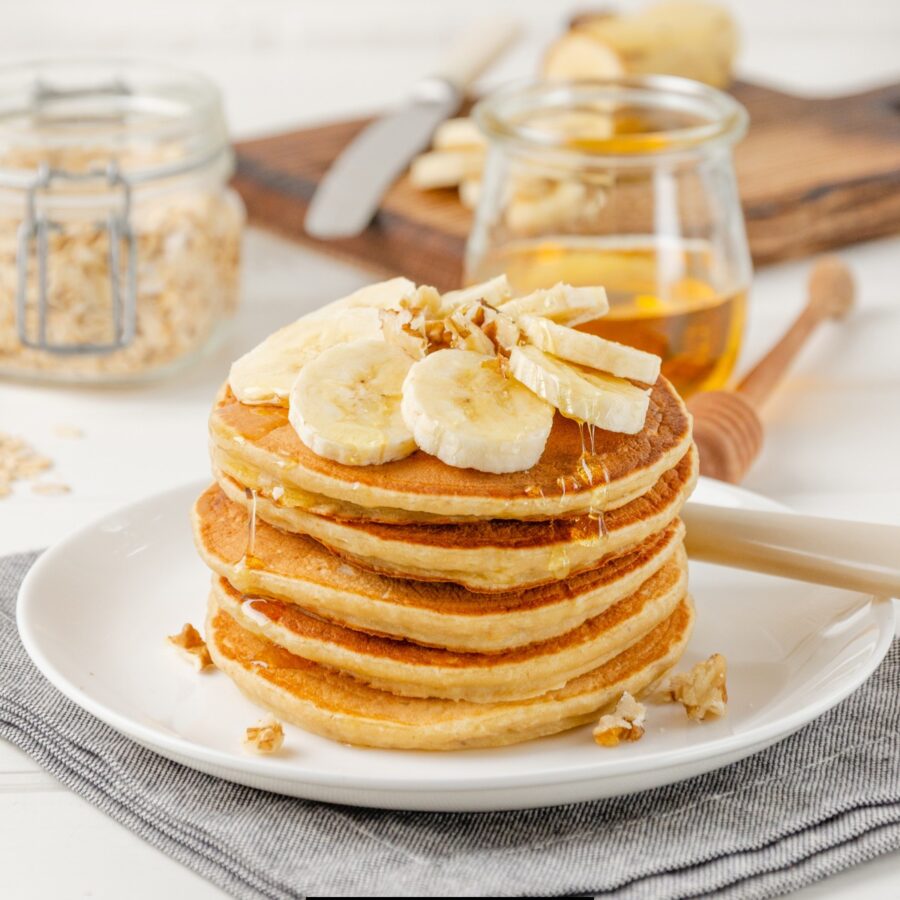 Banana Oatmeal Pancakes on a white plate topped with fresh bananas and syrup