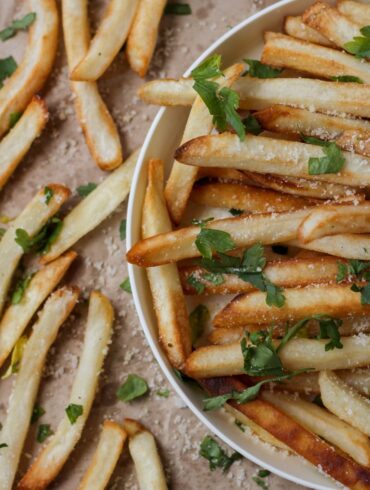 Close up image of Oven Baked Fries in a bowl and on brown parchment paper next to it