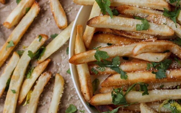 Close up image of Oven Baked Fries in a bowl and on brown parchment paper next to it