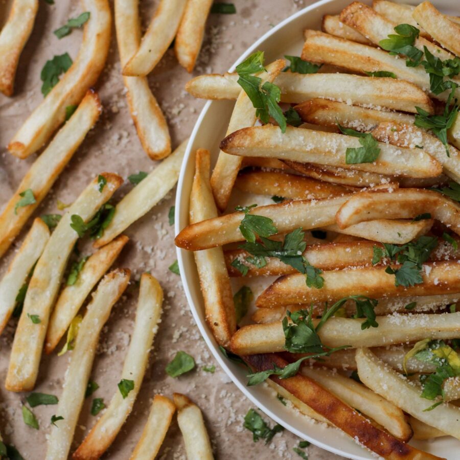 Close up image of Oven Baked Fries in a bowl and on brown parchment paper next to it