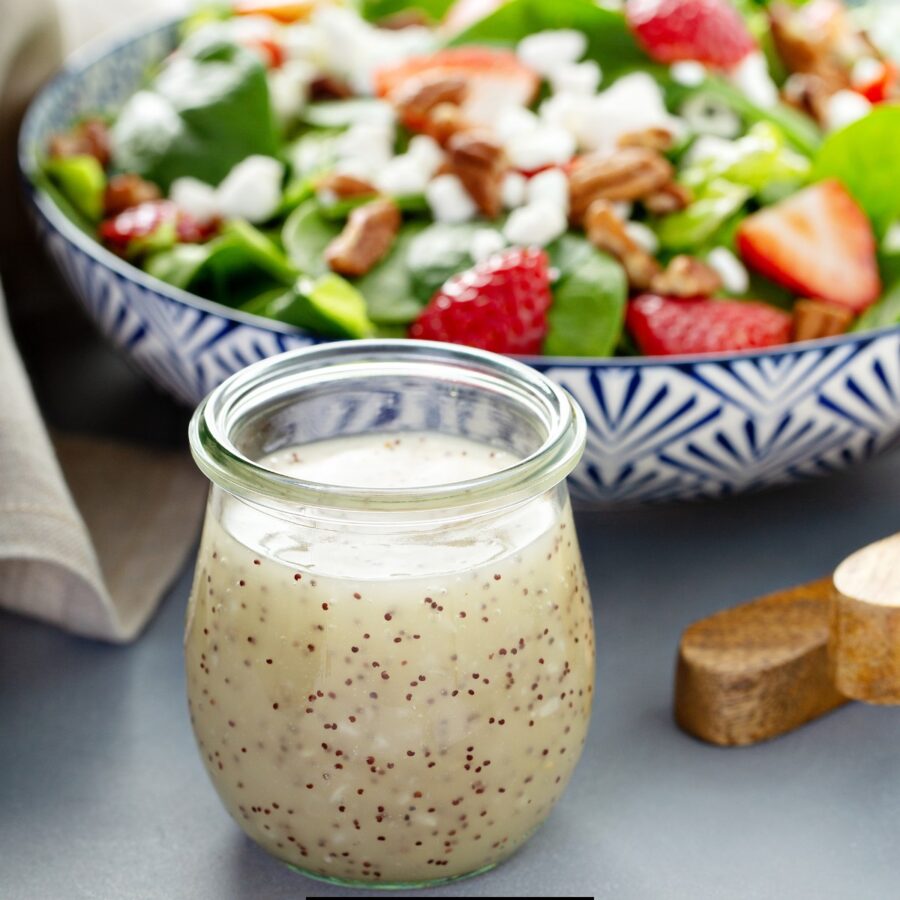 A glass jar of Poppyseed Dressing in front of a fresh salad