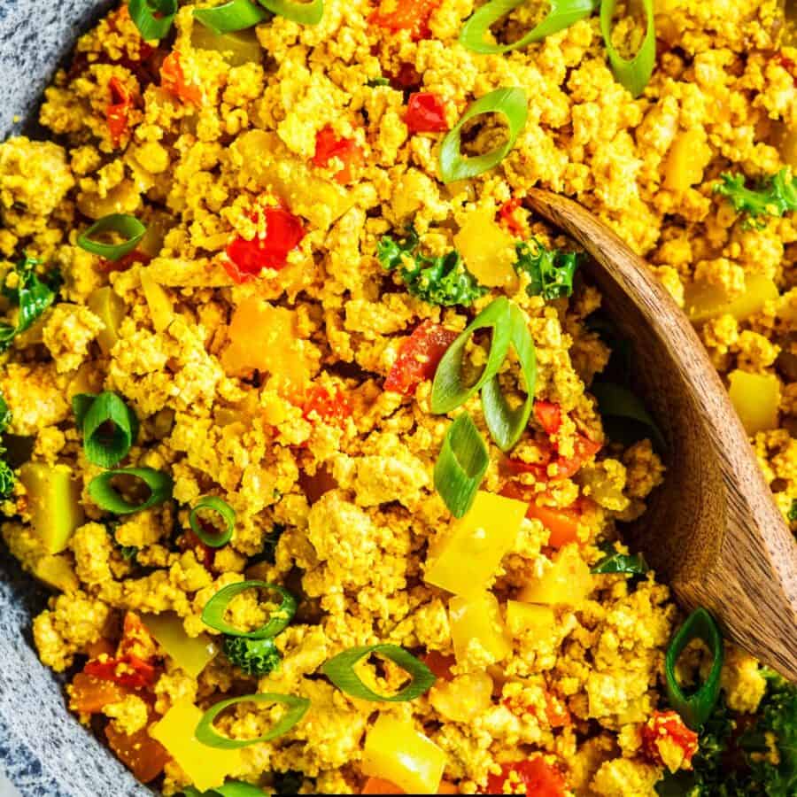 Close up image of tofu scramble in a pan with a wooden serving spoon