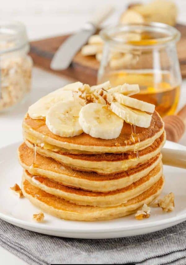 Banana Oatmeal Pancakes on a white plate topped with fresh bananas and syrup