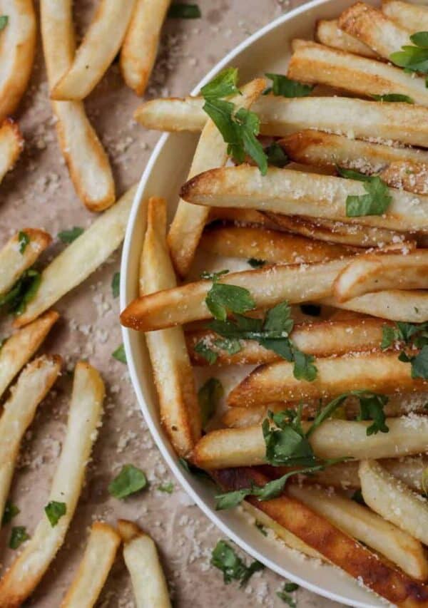 Close up image of Oven Baked Fries in a bowl and on brown parchment paper next to it