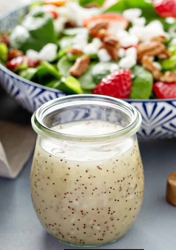 A glass jar of Poppyseed Dressing in front of a fresh salad