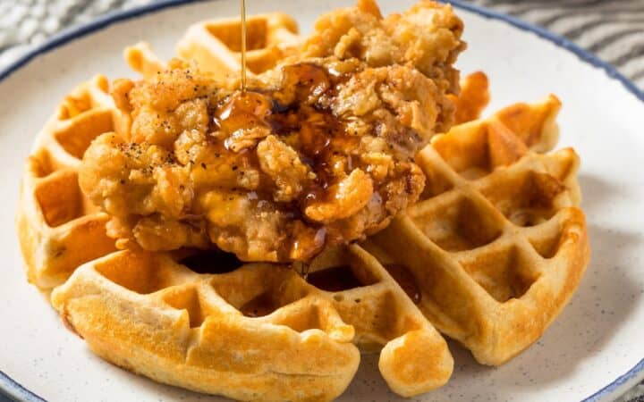 A buttermilk waffl on a white plate with a piece of fried chicken and syrup