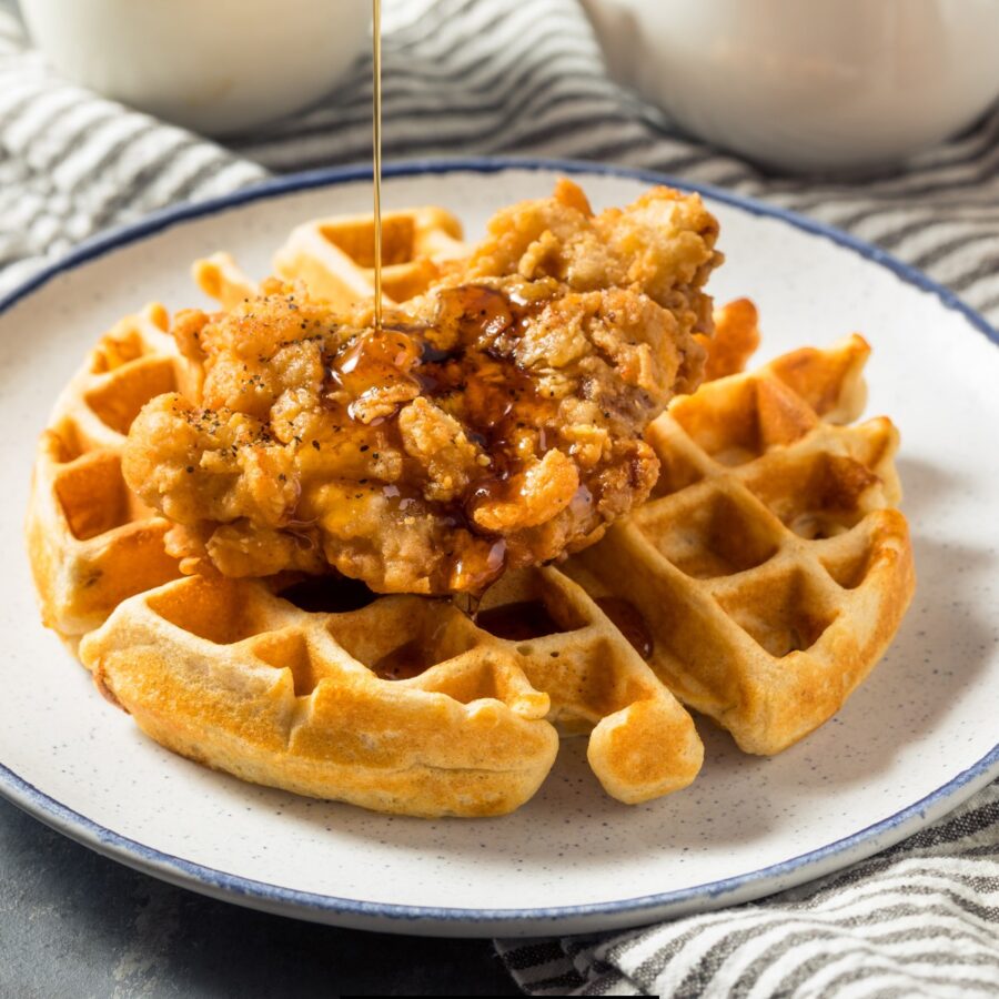 A buttermilk waffl on a white plate with a piece of fried chicken and syrup