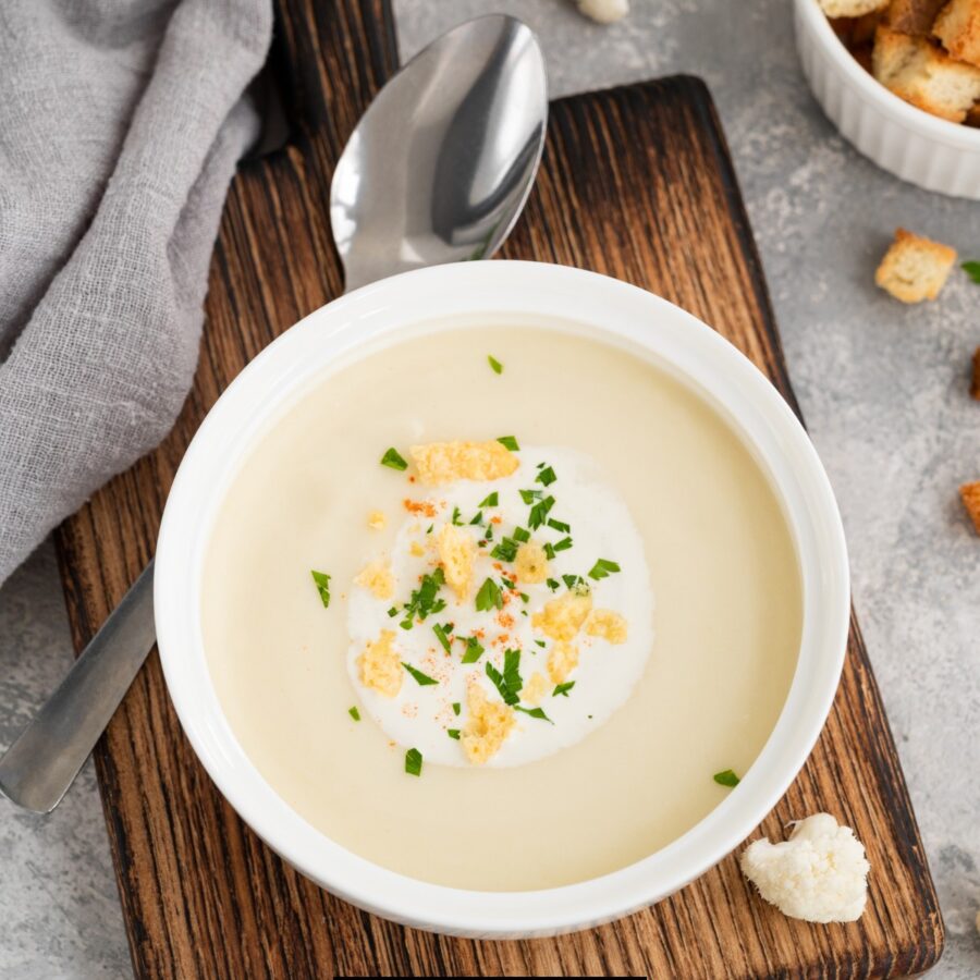 Overhead image of cauliflower cheese soup in a white bowl