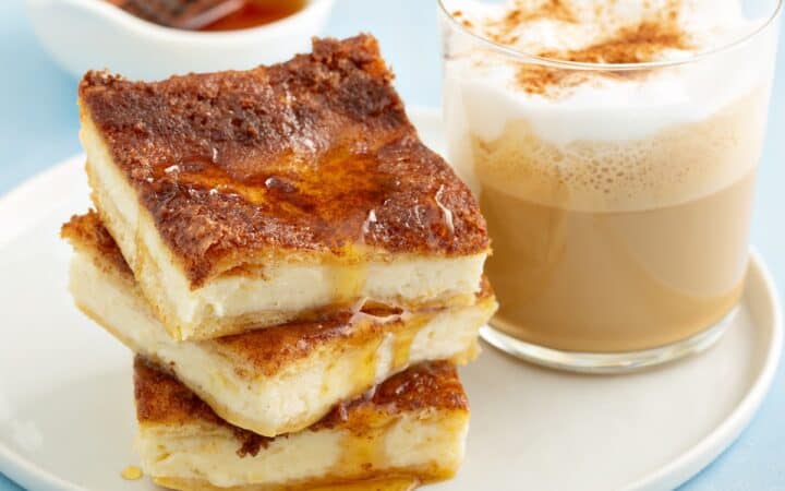 Close up image of three cheesecake bars stacked on a plate with a drink next to them