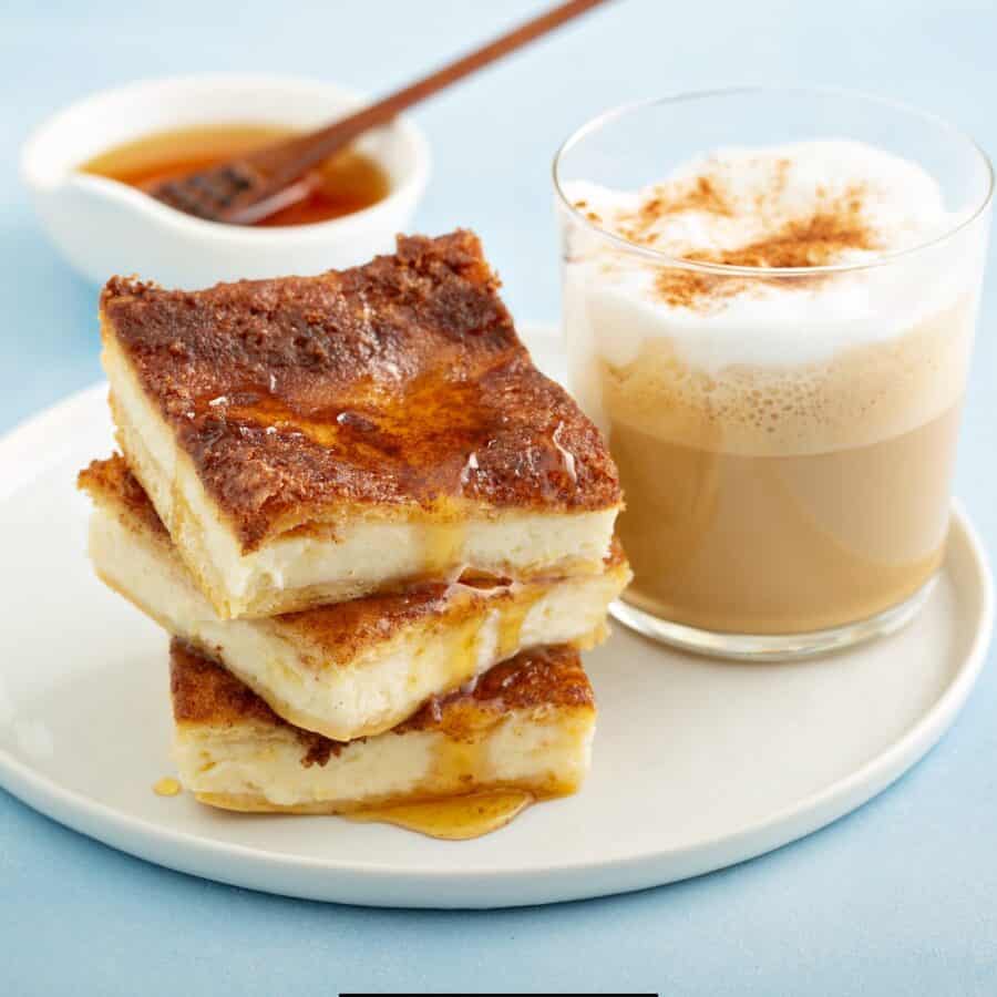 Close up image of three cheesecake bars stacked on a plate with a drink next to them