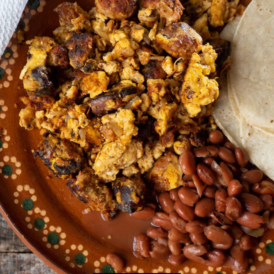 Overhead image of Chorizo and Eggs on a brown plate with beans and tortillas