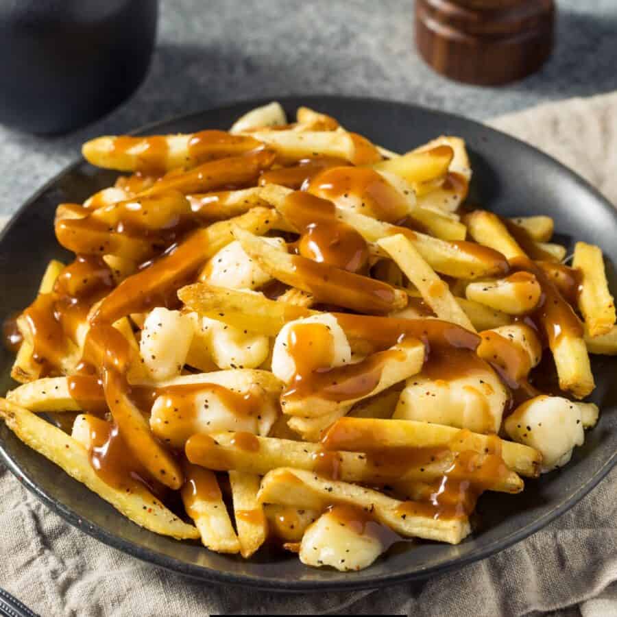 Close up image of homemade poutine on a black plate against a rustic backdrop