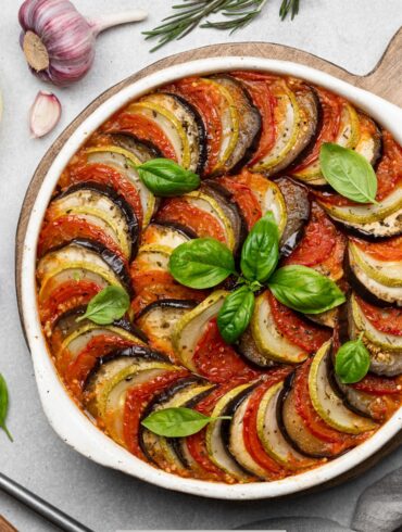 Overhead image of Layered Ratatouille in a white dish with ingredients surrounding it