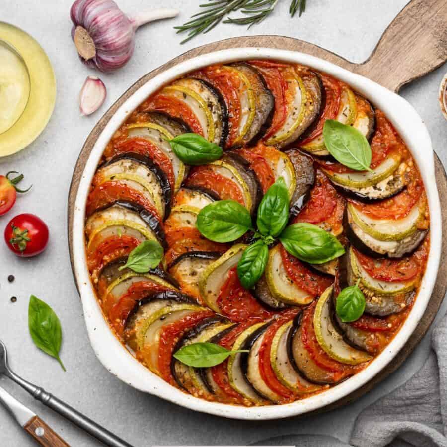 Overhead image of Layered Ratatouille in a white dish with ingredients surrounding it