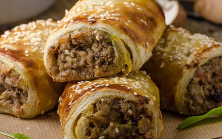 Close up image to sausage rolls stacked on parchment paper