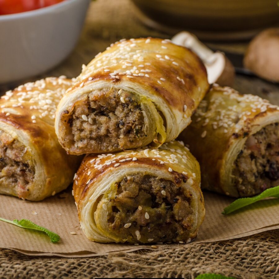 Close up image to sausage rolls stacked on parchment paper