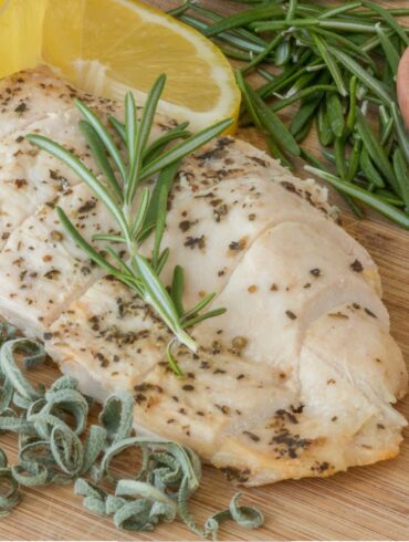 Overhead image of a Sous Vide Chicken Breast surrounded by herbs and lemon wedges