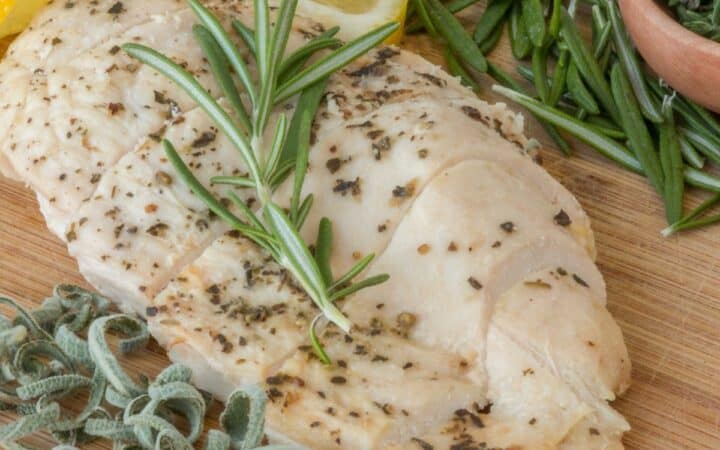 Overhead image of a Sous Vide Chicken Breast surrounded by herbs and lemon wedges