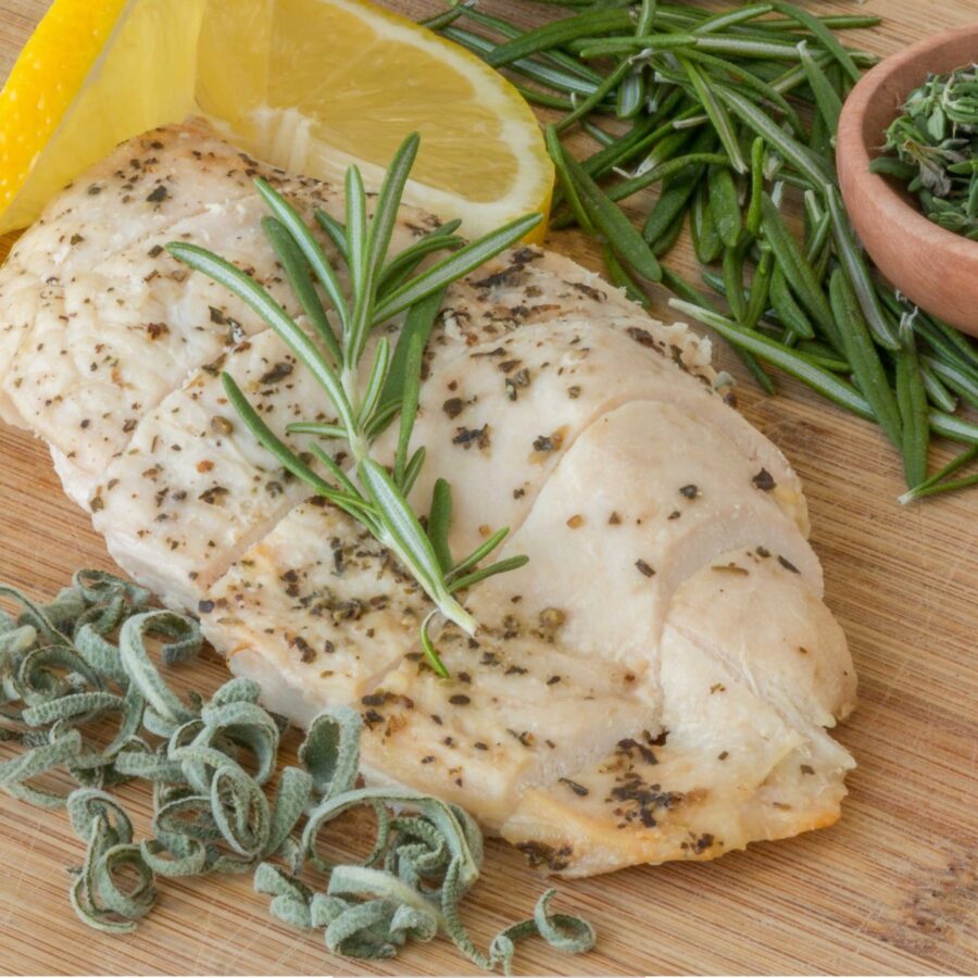 Overhead image of a Sous Vide Chicken Breast surrounded by herbs and lemon wedges