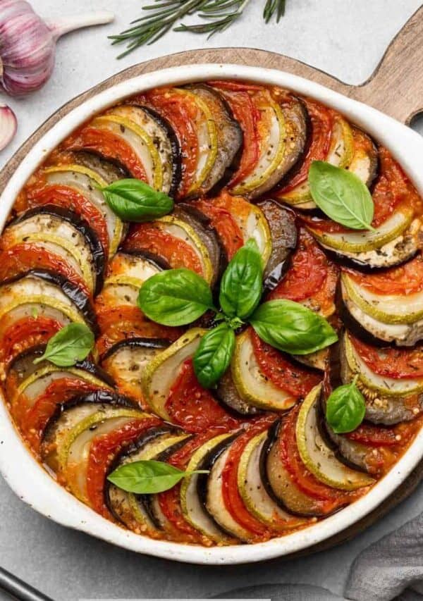 Overhead image of Layered Ratatouille in a white dish with ingredients surrounding it