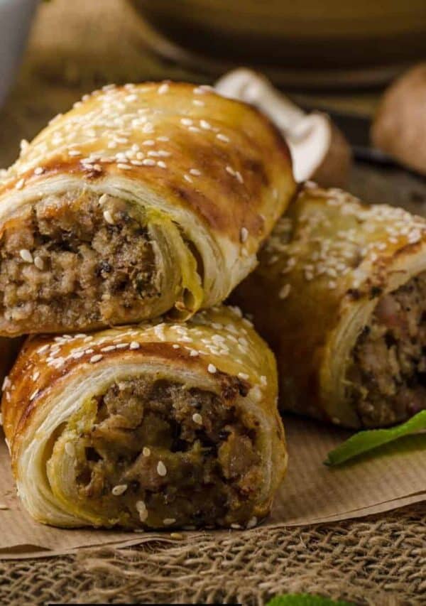 Close up image to sausage rolls stacked on parchment paper