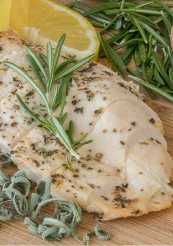 Overhead image of a Sous Vide Chicken Breast surrounded by herbs and lemon wedges