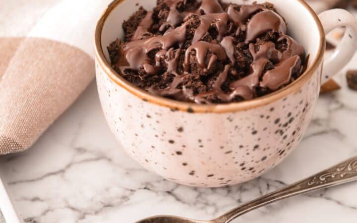 A coffee mug cake on a marble counter top with a spoon next to it