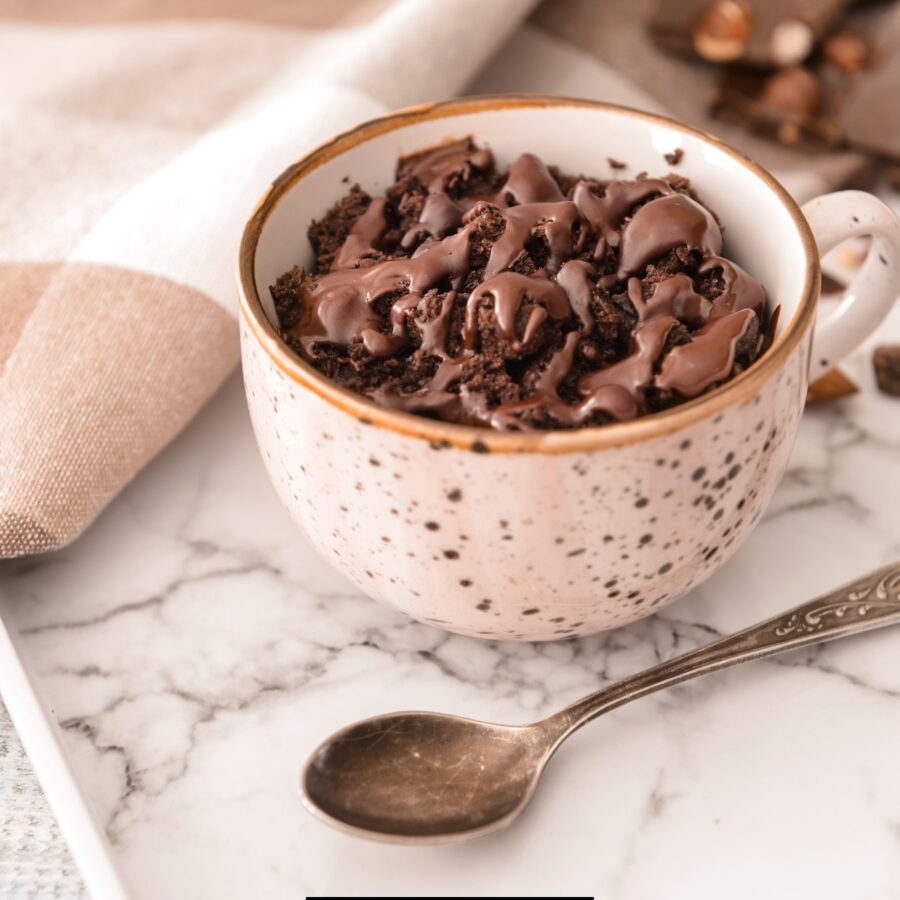 A coffee mug cake on a marble counter top with a spoon next to it